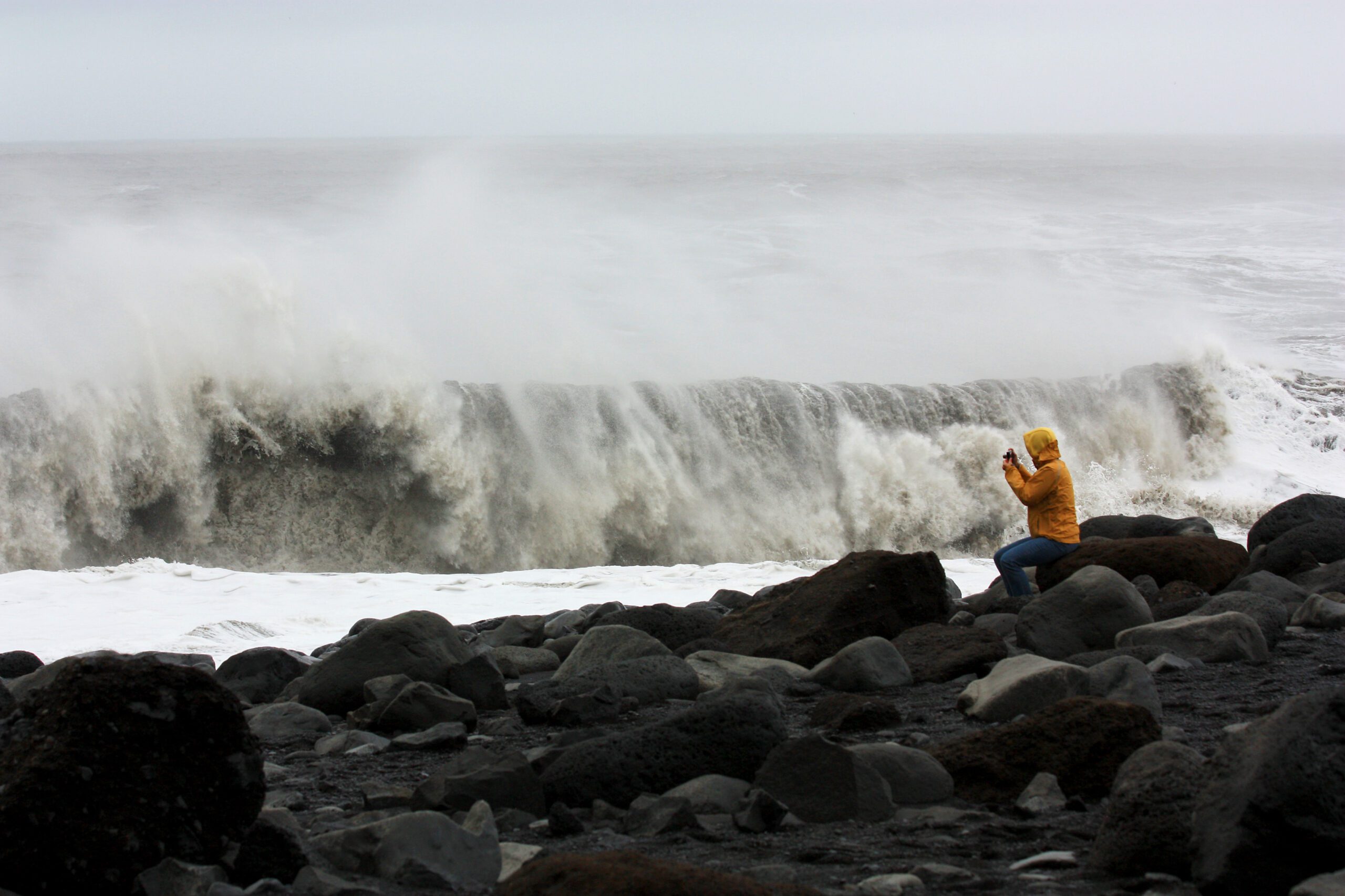Billede af en fotograf, som tager billede af en bølge på den Sorte Strand på Island.