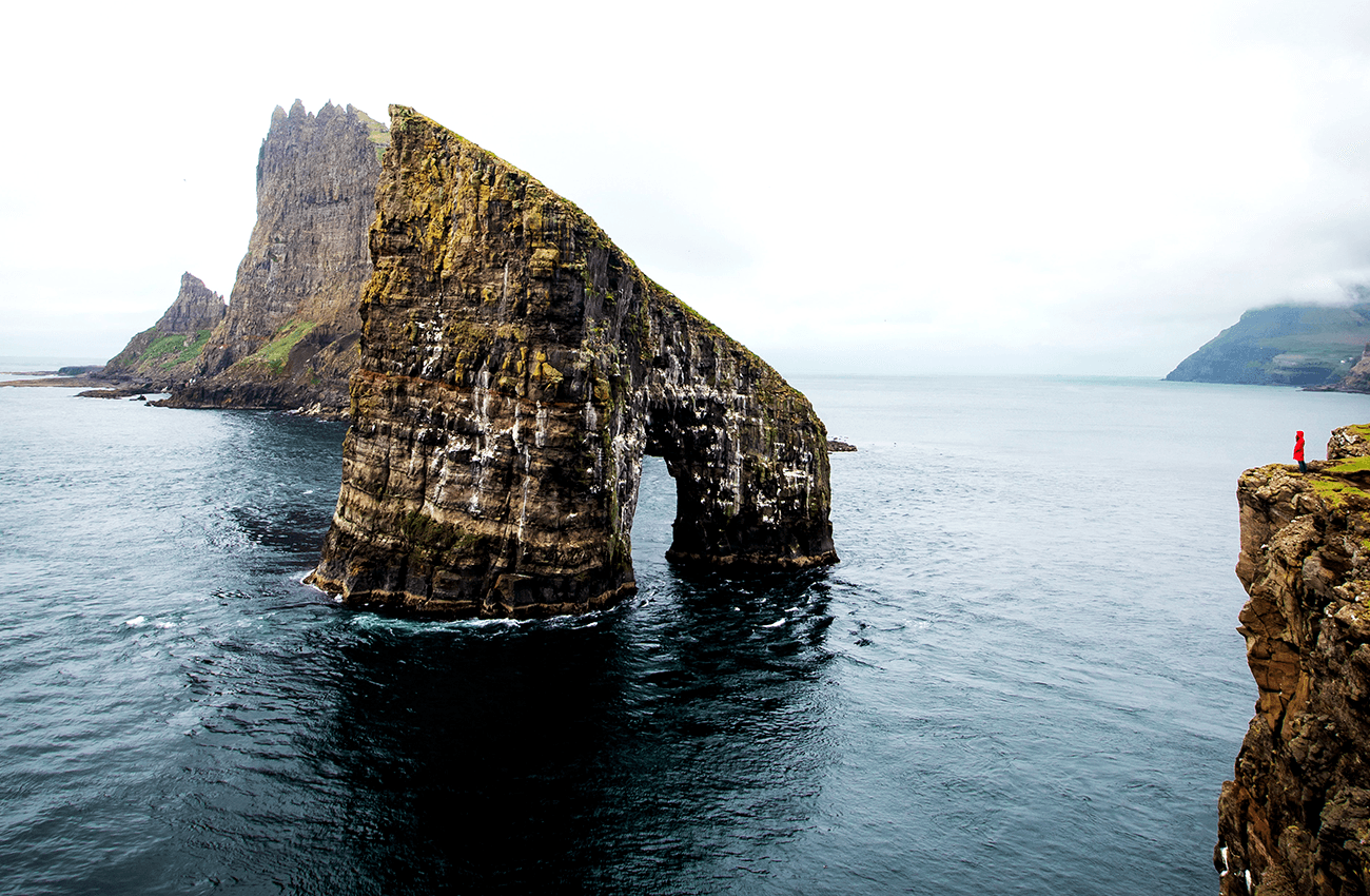 Billede af en stor klippe ude i havet på Færøerne.,