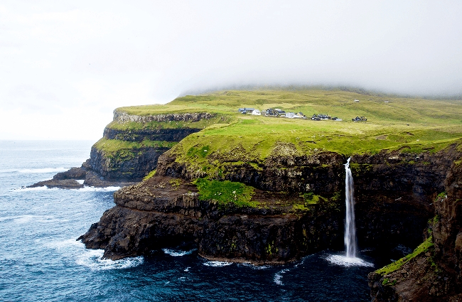 Billede af vandfaldet Gasadalur, der går ud til vandet med huse i baggrunden på Færøerne.