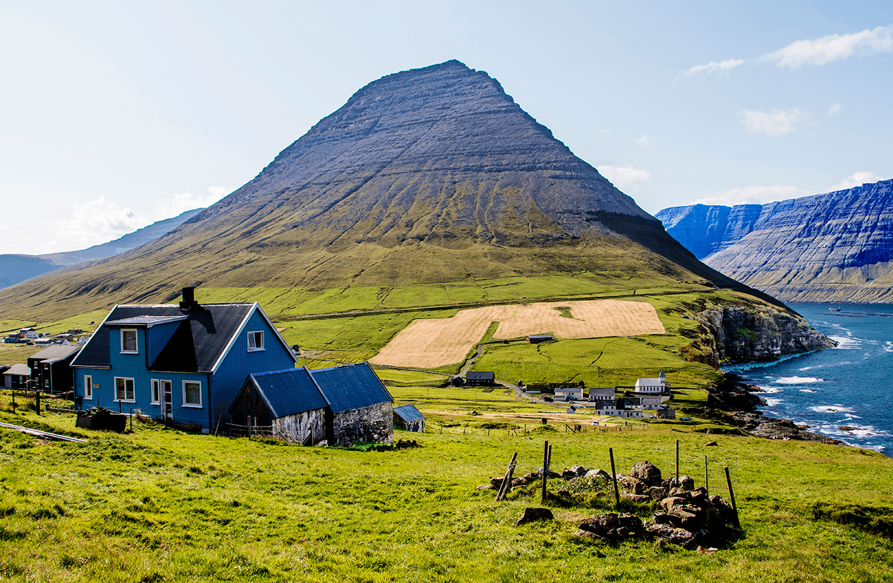 Billede af nogle huse og en mark på siden af et bjerg på Færøerne.