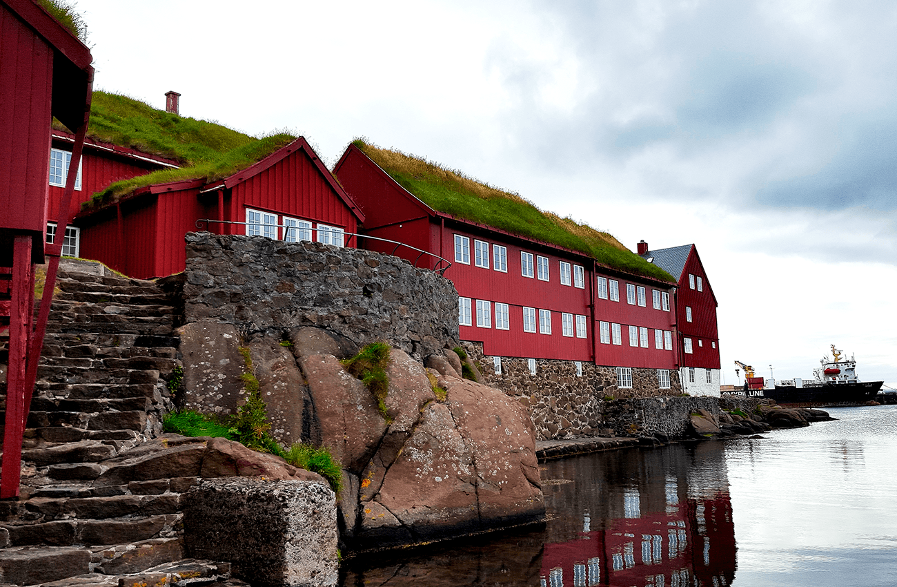 Billede af nogle røde huse med mos på tagene i Torshavns havn på Færøerne.