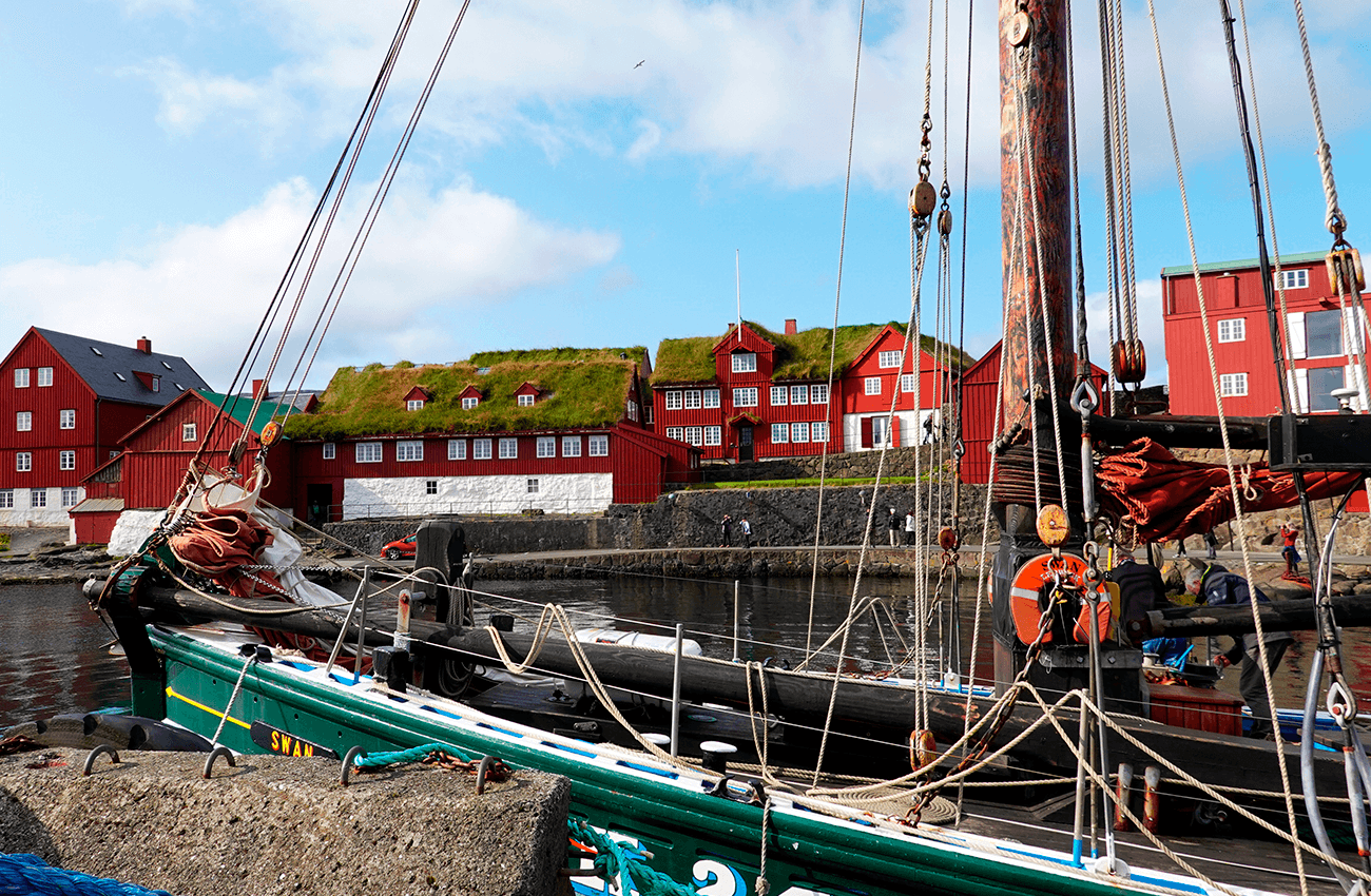 Billede af en båd med røde huse med mos på tagene i Torshavn på Færøerne.