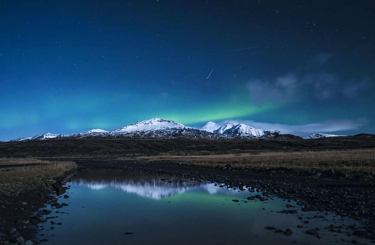 Billede af Thorsmork's bjerge med sne på toppen og nordlys over bjergene på Island.