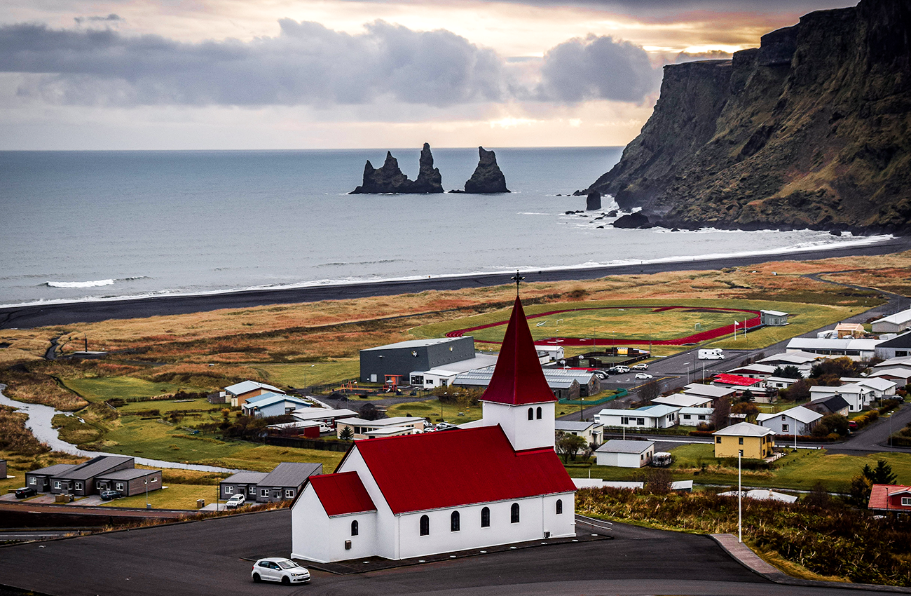 Billede af en kirke i Vik på Island, med udsigt til en sort strand og klipper ude i vandet.