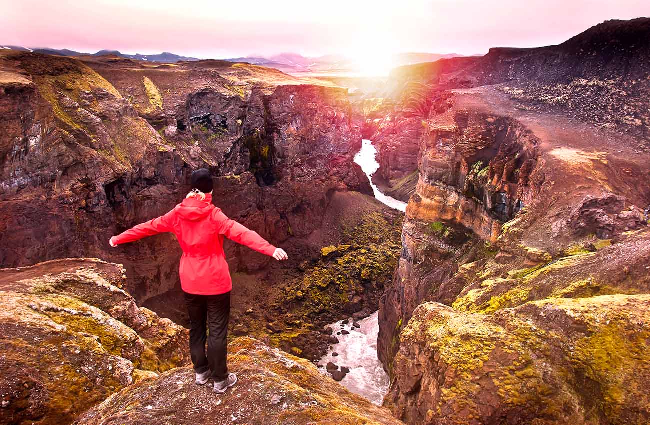 Billede af en turist som står over kløften Markarfljotsgljufur med smuk solnedgang i baggrunden.