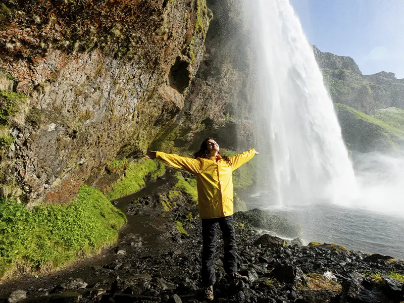 Kvinder står under Seljalandfoss og ser glad ud med udstrakte arme