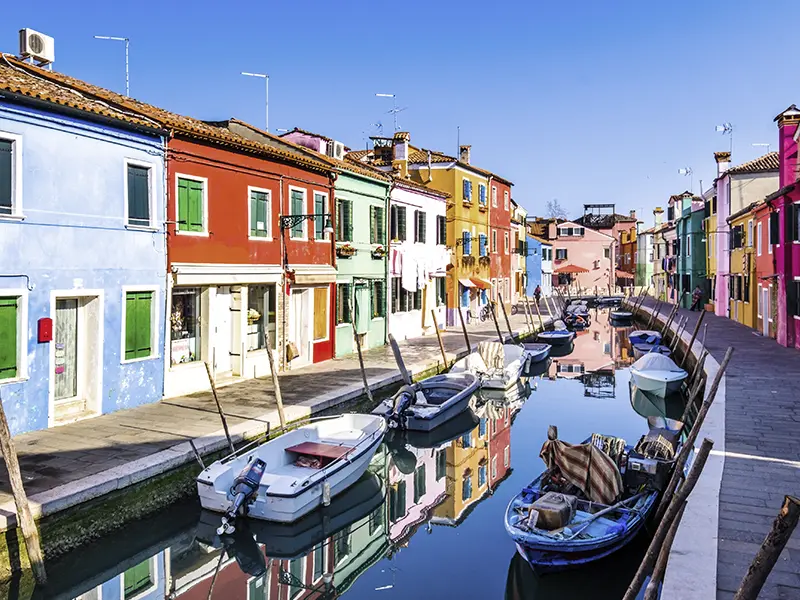 Farverige huse og små både langs en kanal på øen Burano ved Venedig.