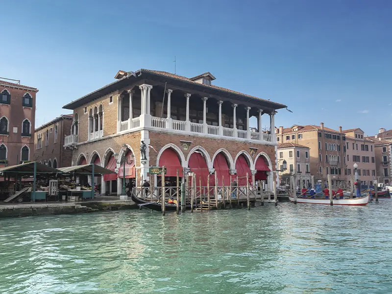 Rialto-markedet i Venedig med den nygotiske markedshal, røde markiser og udsigt over kanalen.