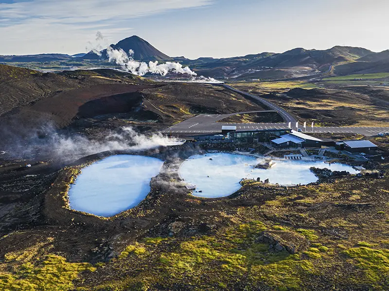 blå lagune med dampende vand mellem bjerge og lava